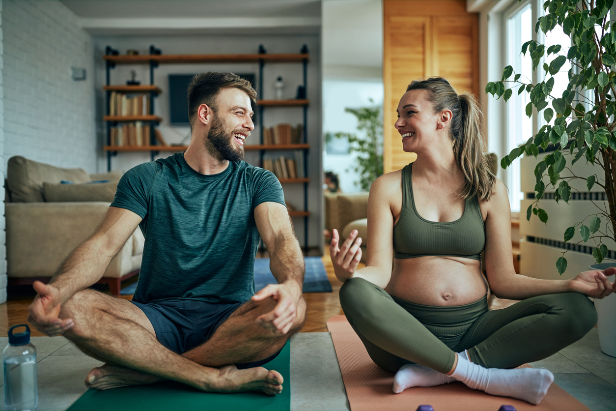 Pregnant young woman practicing yoga with her husband at home